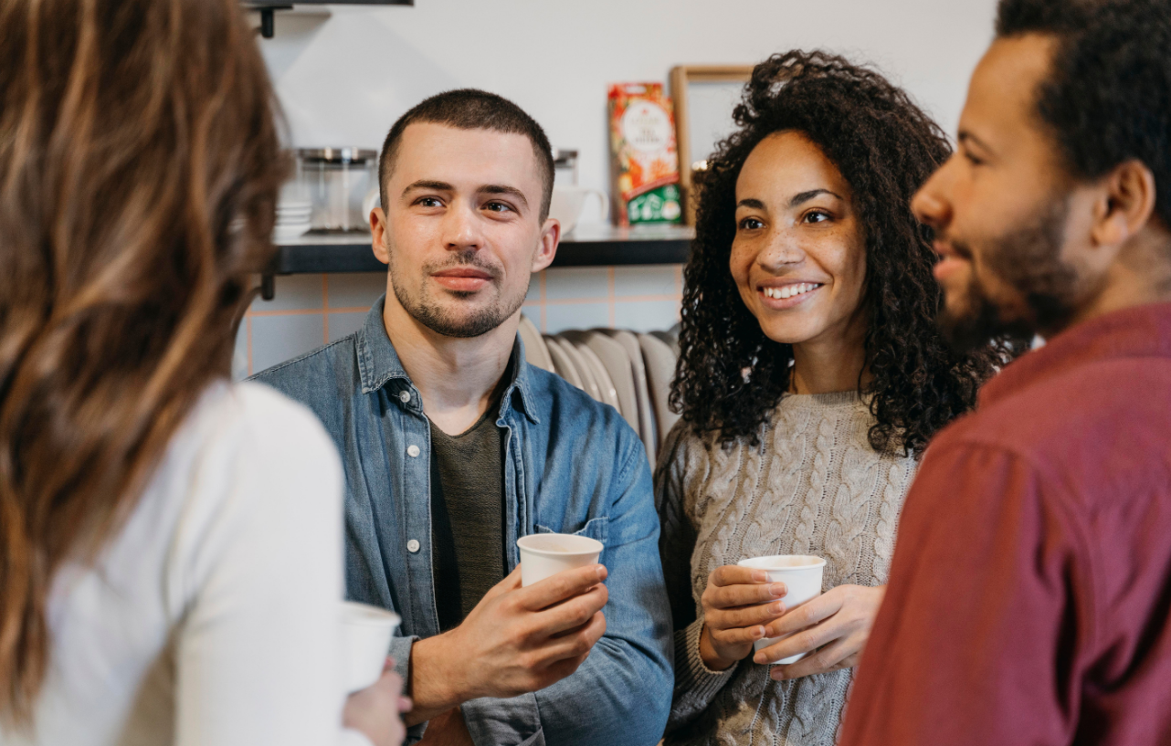 Grupo de pessoas conversando e segurando copos de café, representando uma troca de ideias e conhecimento.