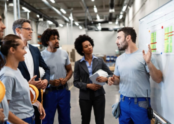 Equipe de trabalho em uma fábrica discutindo resultados e gráficos com gestores.