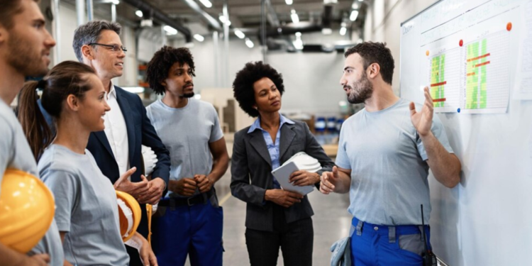 Equipe de trabalho em uma fábrica discutindo resultados e gráficos com gestores.