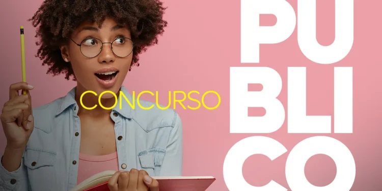 Pessoa com cabelo cacheado, óculos e camisa azul segurando um lápis, com expressão de surpresa, em frente a um fundo rosa, em uma imagem sobre concursos públicos.