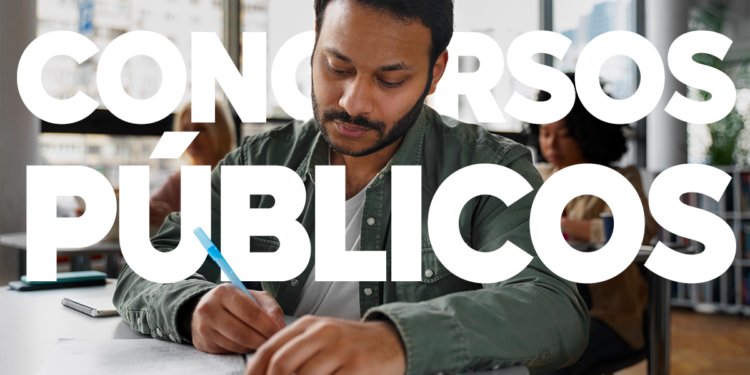 Homem escrevendo em um caderno enquanto estuda para um concurso público, em um ambiente de biblioteca.