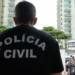 Policial civil com uniforme, com as palavras 'POLÍCIA CIVIL' estampadas nas costas, próximo à entrada da delegacia