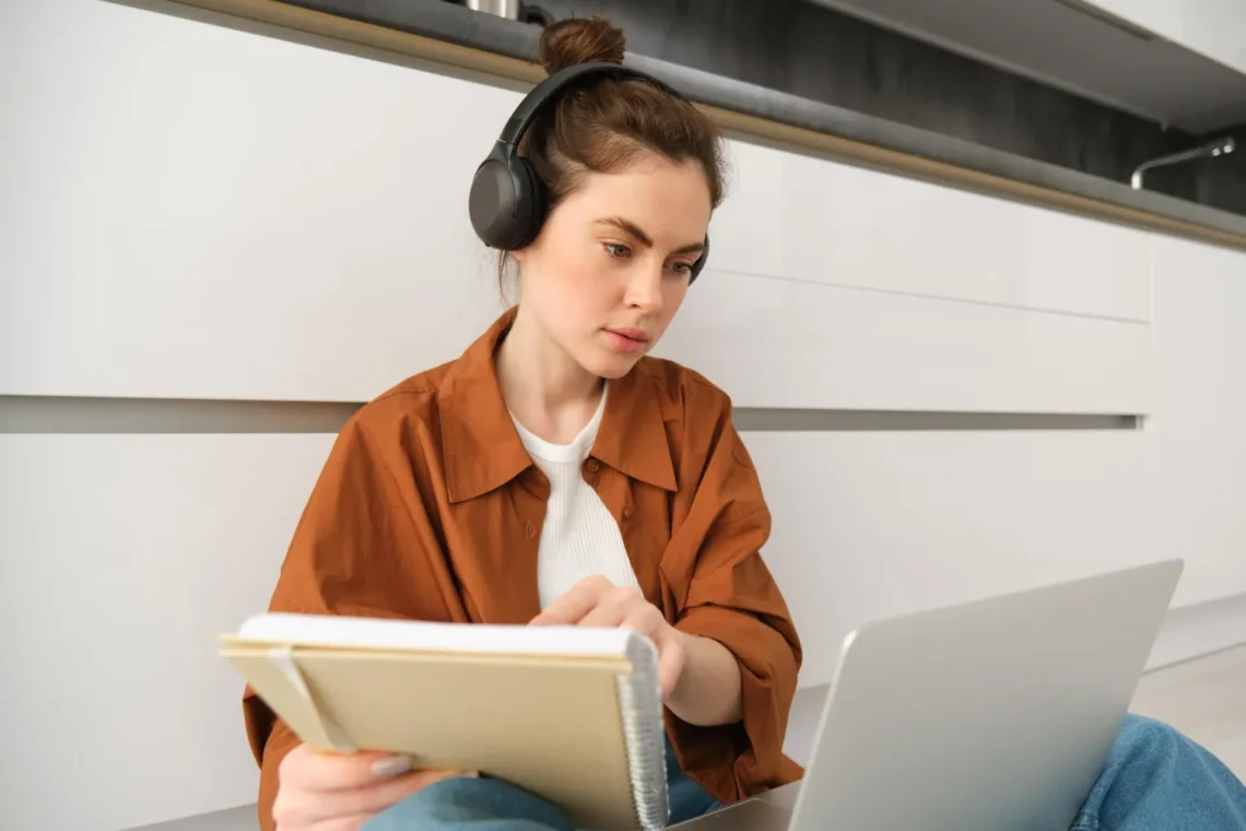 Jovem estudando com fones de ouvido, caderno e laptop, representando a preparação para o CNU 2025