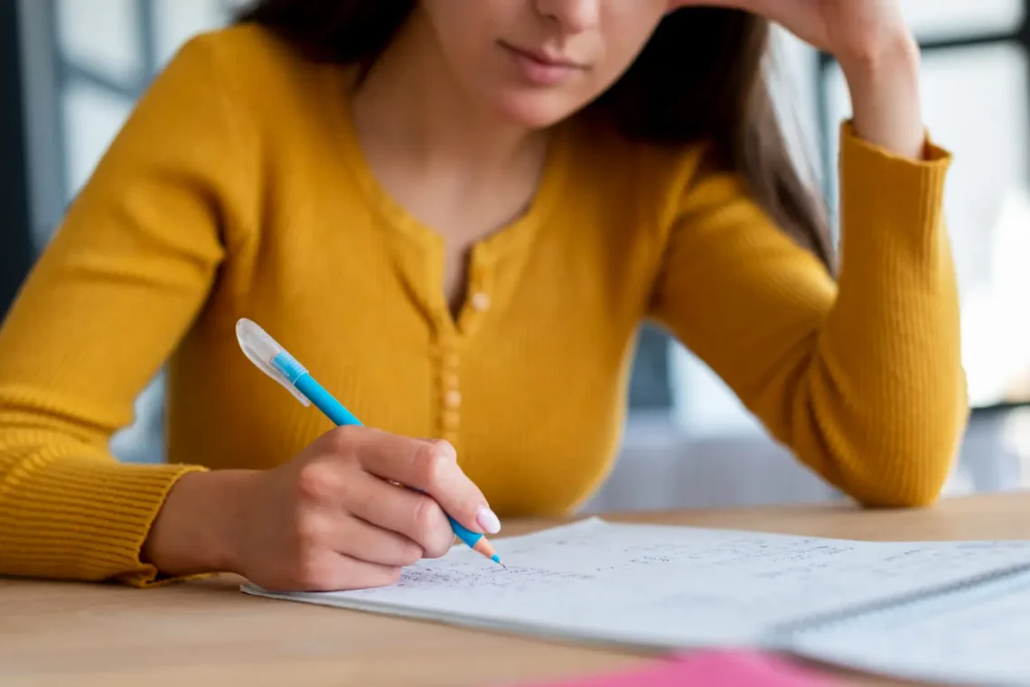 Mulher estudando e fazendo anotações com lápis azul em caderno, representando preparação para concursos