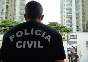 Agente da Polícia Civil de costas, em frente à delegacia.