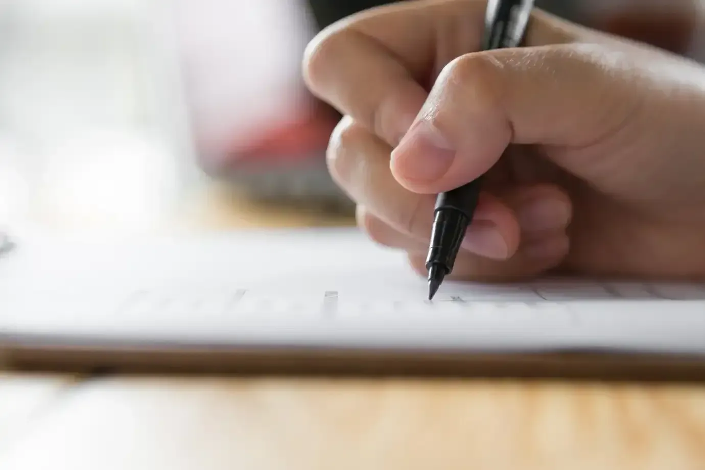 Pessoa escrevendo com uma caneta em um papel, simbolizando o processo de inscrição para o concurso