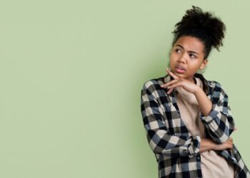 Mulher pensativa com camisa xadrez, refletindo sobre a diferença entre 'de novo' e 'denovo'.