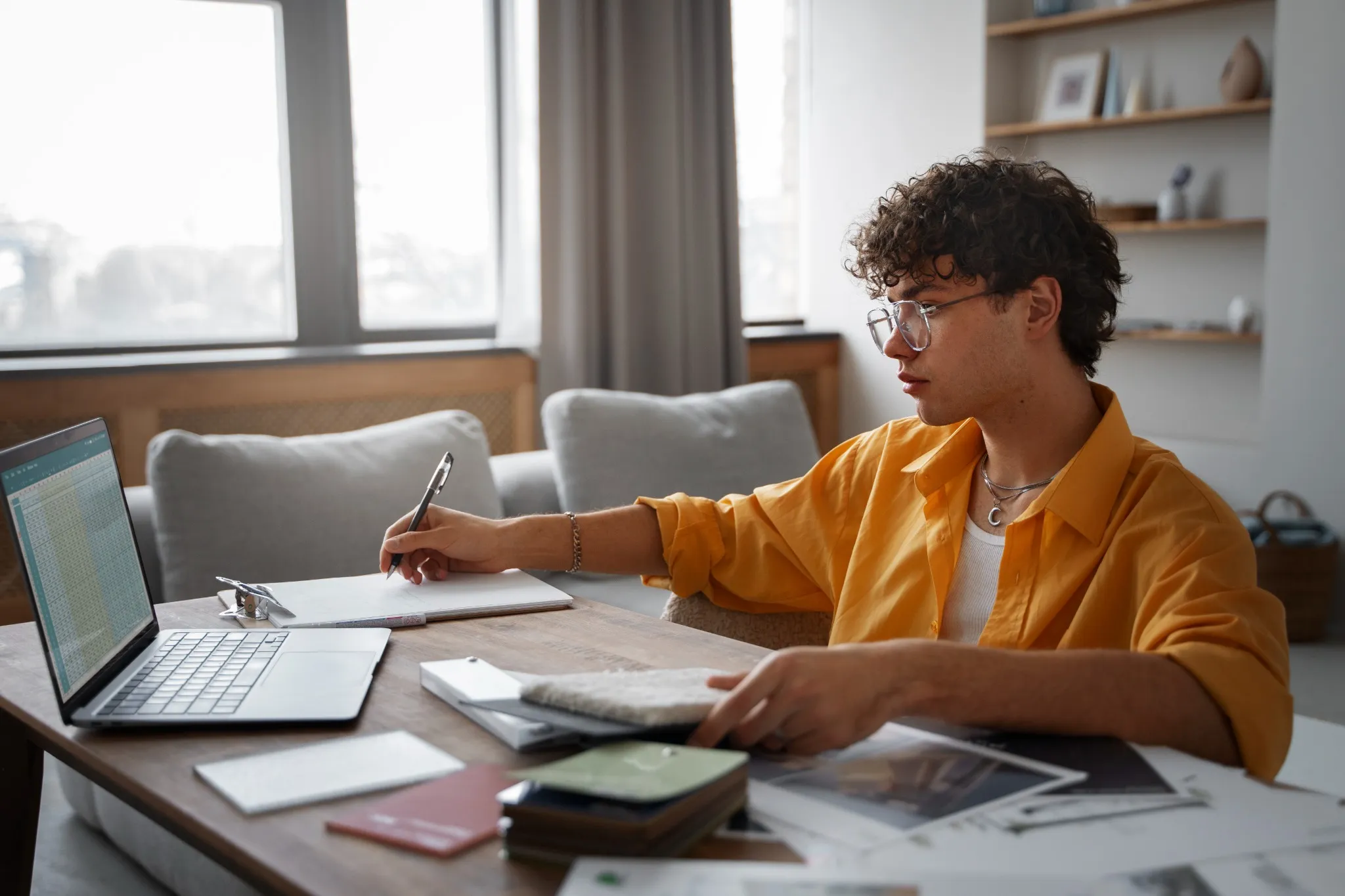 Jovem estudando em casa, analisando documentos e usando um notebook, representando a preparação para concursos públicos.