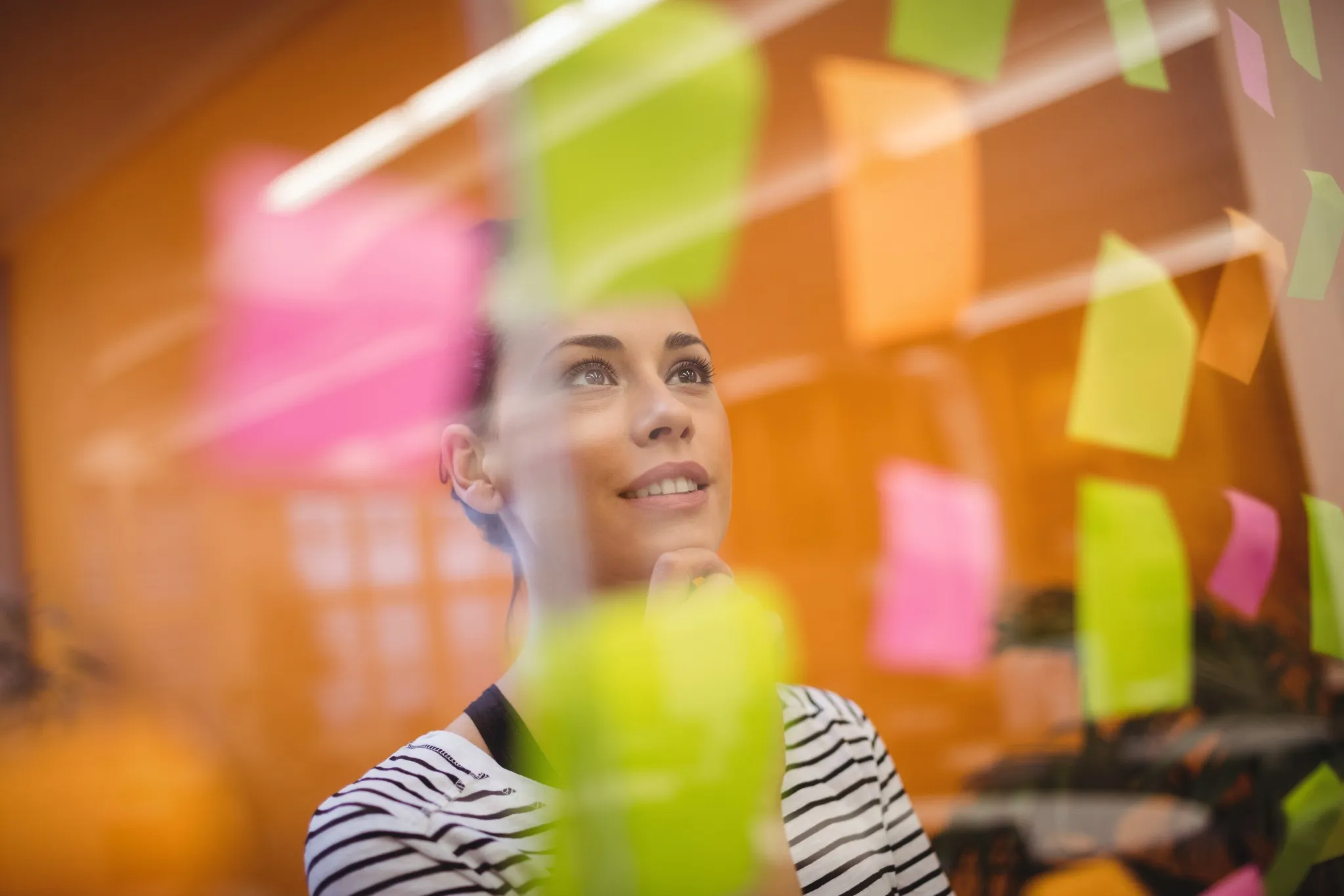 Mulher analisando anotações em post-its coloridos em um ambiente de estudo ou planejamento.