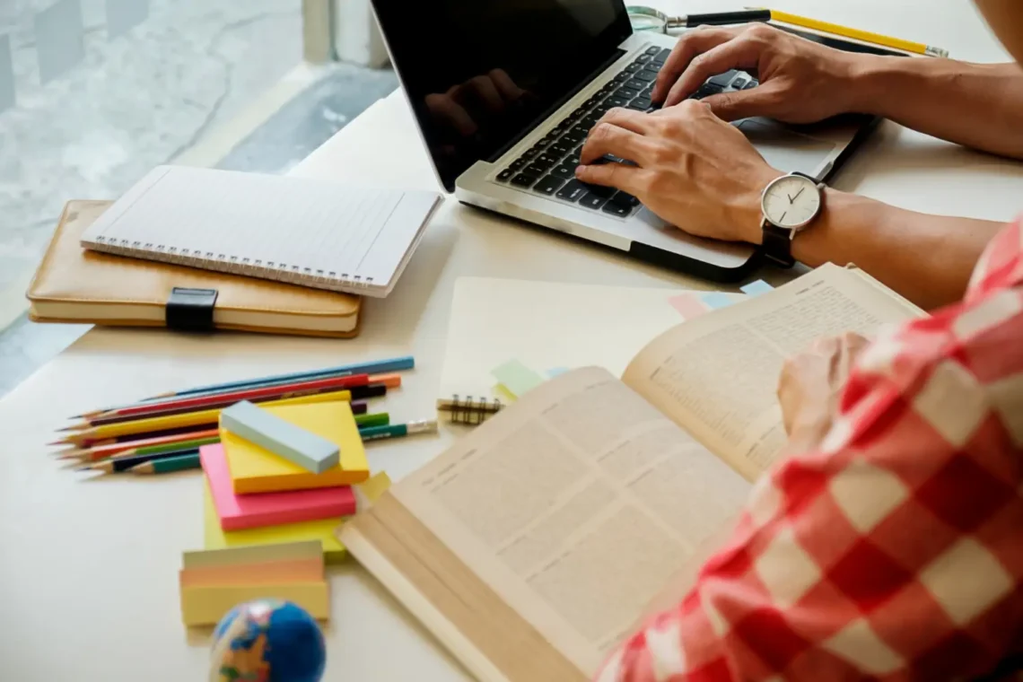 Pessoa estudando para o concurso CBMERJ, com material de estudo e um laptop em sua mesa