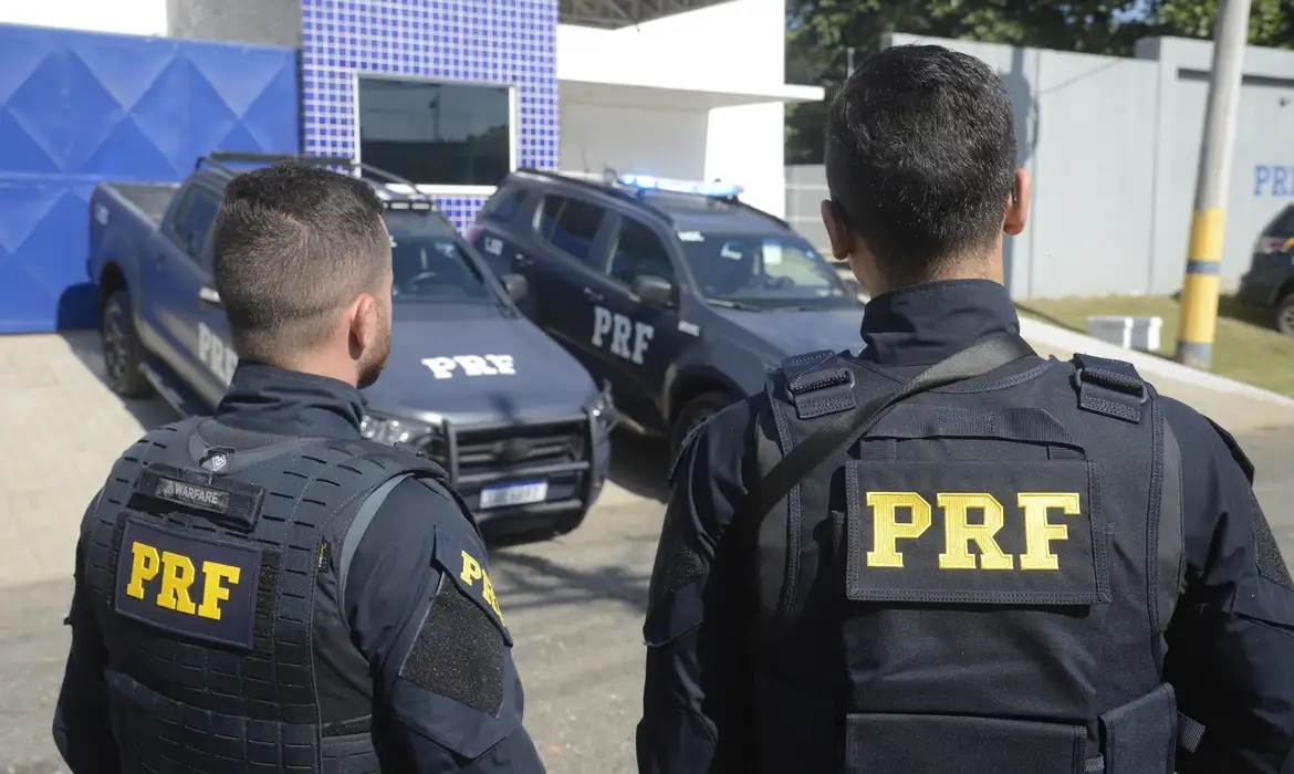 Policiais rodoviários federais em frente a viaturas da PRF, simbolizando a convocação de excedentes.