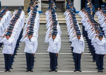 Candidatos em formação militar vestidos com uniformes brancos e prestando continência