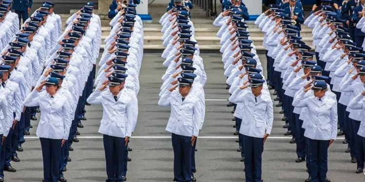 Candidatos em formação militar vestidos com uniformes brancos e prestando continência