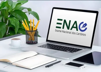 Laptop com a logo do ENAC na tela, acompanhado de materiais de estudo sobre uma mesa organizada