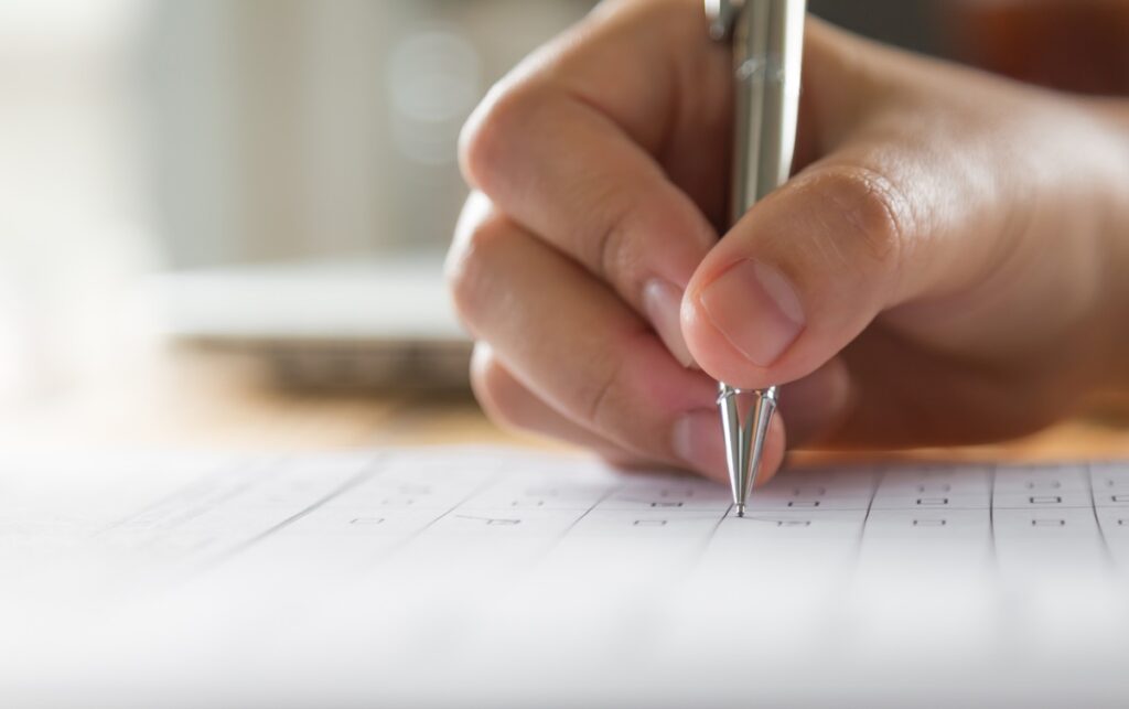  Mão preenchendo um formulário de múltipla escolha, representando o processo de inscrição para o concurso público.