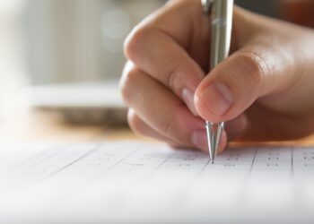 Mão preenchendo formulário de inscrição para processo seletivo, representando a última chance de participar do concurso EBSERH e UFPEL.