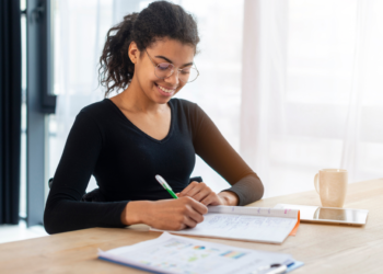 Mulher sorridente estudando em um ambiente tranquilo, fazendo anotações em seu caderno, fazendo referência a como se preparar para concurso.