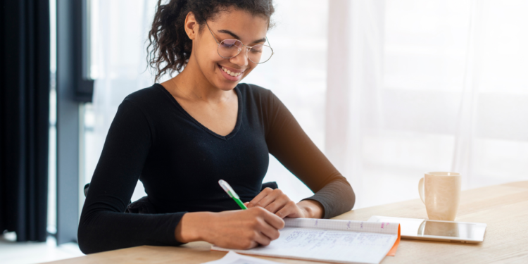 Mulher sorridente estudando em um ambiente tranquilo, fazendo anotações em seu caderno, fazendo referência a como se preparar para concurso.