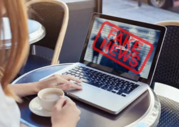 Pessoa verificando informações em um laptop com alerta de 'Fake News' sobre o CNU 2025