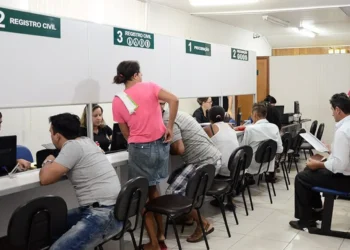 Pessoas atendendo em um cartório, com mesas e balcões organizados, representando o processo de registro civil.