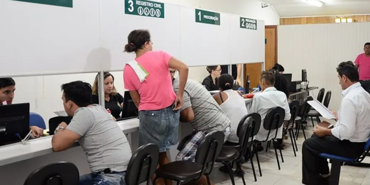 Pessoas atendendo em um cartório, com mesas e balcões organizados, representando o processo de registro civil.