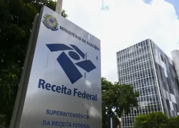 Placa da Receita Federal com o logo e o edifício da instituição ao fundo, localizada no Ministério da Fazenda.