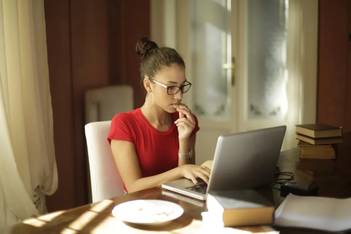 Jovem estudante concentrada revisando materiais no notebook enquanto se prepara para o Concurso Nacional Unificado 2025