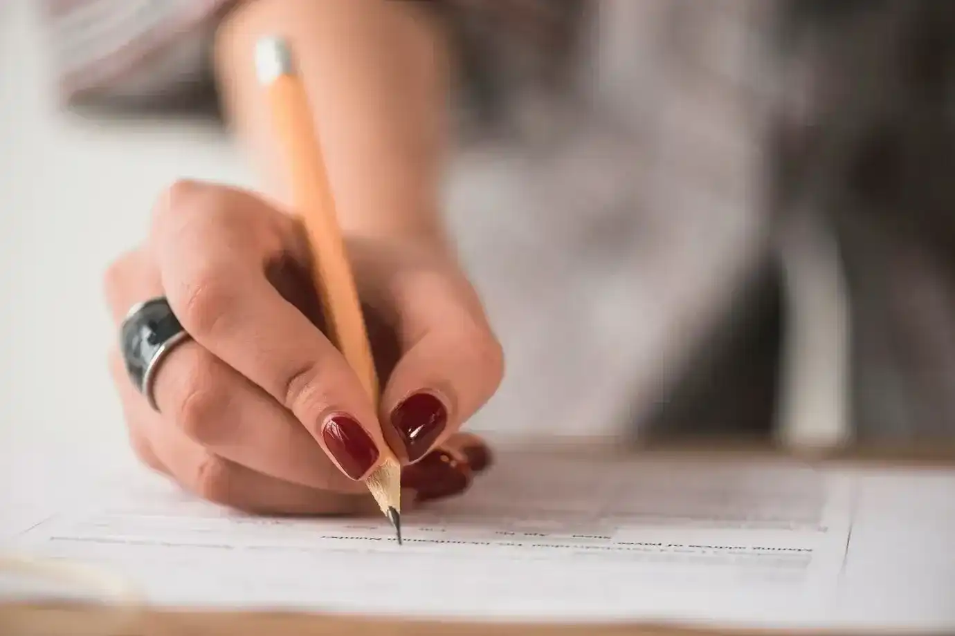 Mão segurando lápis e preenchendo um formulário, representando a participação em concursos públicos.