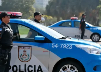Policiais militares do RJ ao lado de viaturas azuis estacionadas.