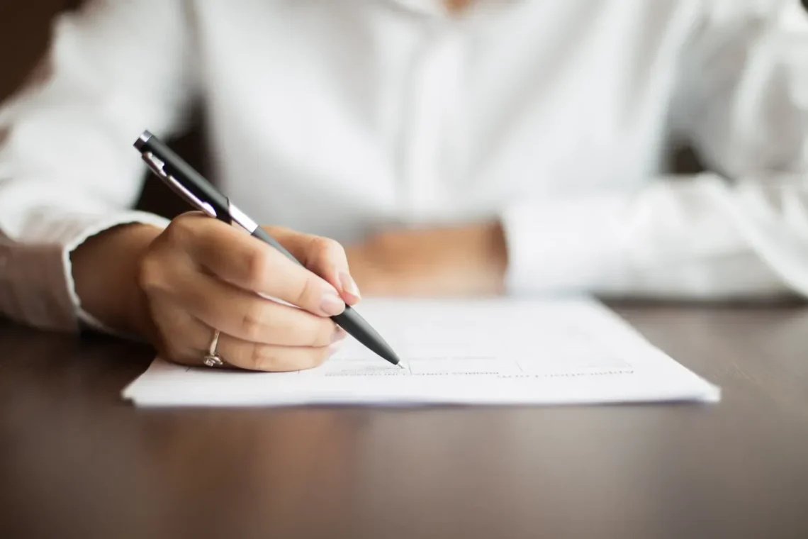 Pessoa escrevendo em um documento, representando a preparação para um concurso público