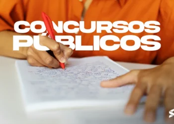 Mãos segurando uma caneta vermelha enquanto escreve em um caderno, representando a preparação para concursos públicos