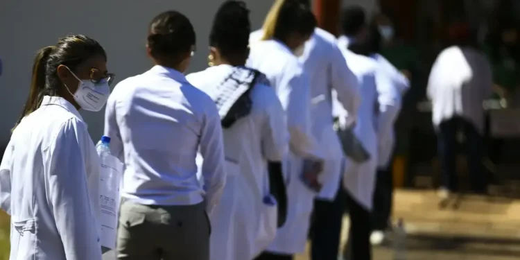 Profissionais da saúde em fila para prova de concurso público.