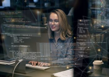 Mulher programadora digitando em frente a um computador com códigos sobrepostos