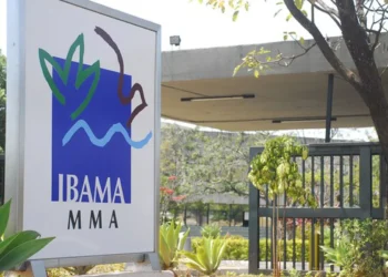 Placa do IBAMA em frente à sede da instituição, com árvores e plantas ao redor.