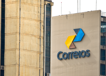 Logo dos Correios em um prédio, com cores amarelo, azul e cinza no design.