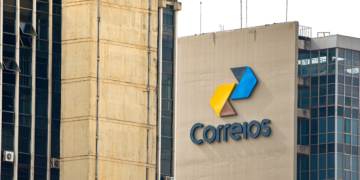 Logo dos Correios em um prédio, com cores amarelo, azul e cinza no design.