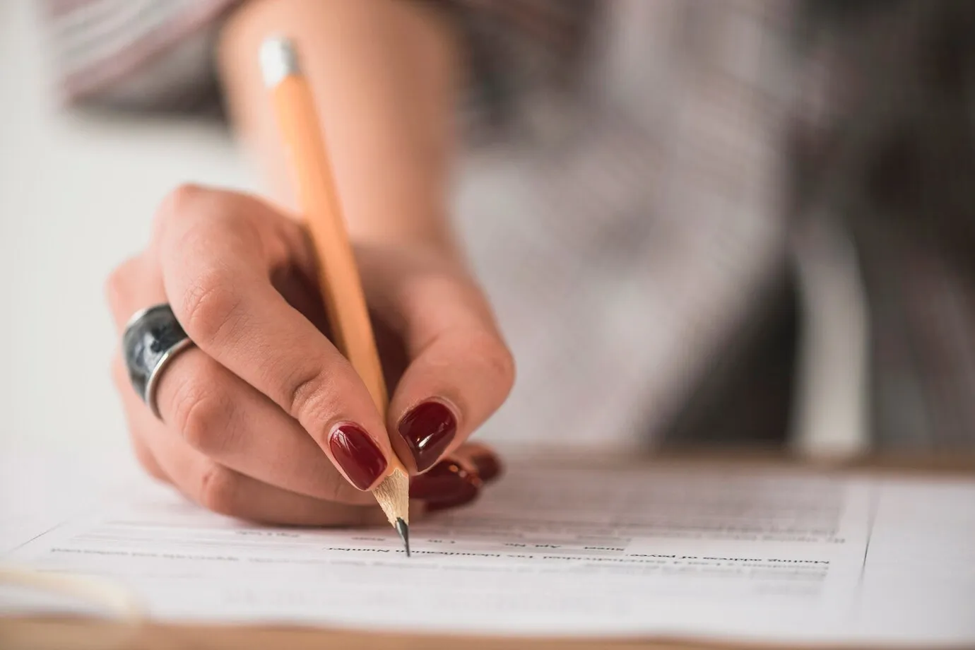  Pessoa escrevendo com lápis em formulário de concurso, simbolizando o processo de avaliação.