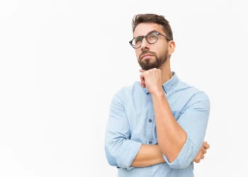 Homem pensativo com barba e óculos, olhando para cima enquanto reflete sobre algo importante.