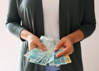 Pessoa segurando cédulas de dinheiro, incluindo notas de 100 e 20 reais, representando finanças e economia.