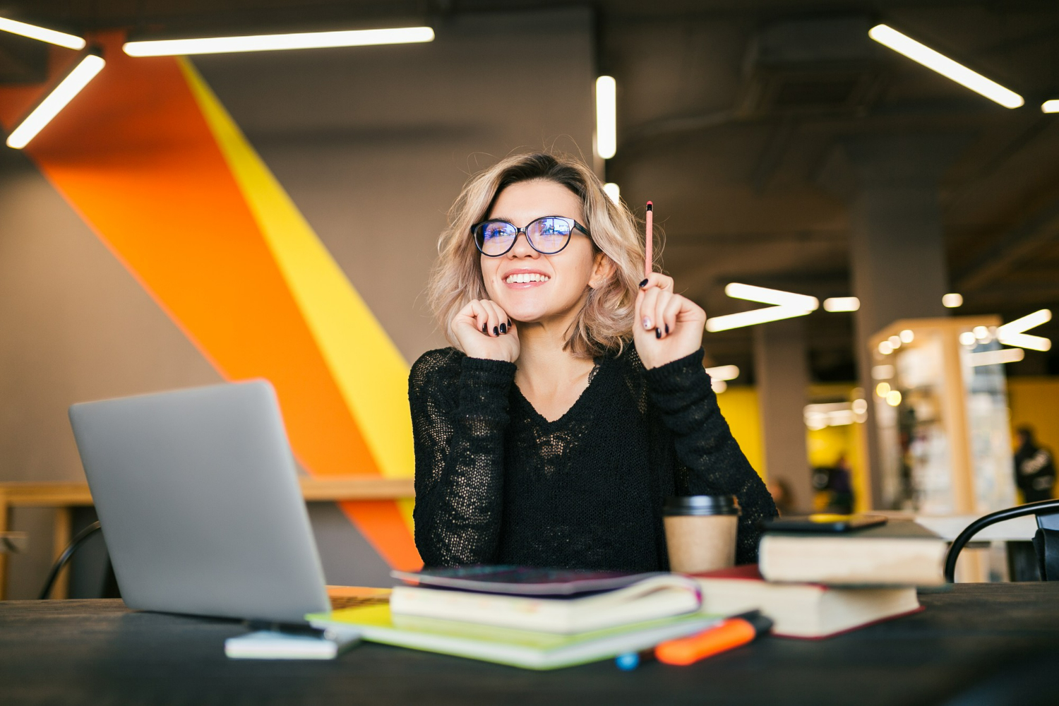Mulher sorridente estudando e refletindo em um ambiente moderno, transmitindo positividade e calma no trabalho.