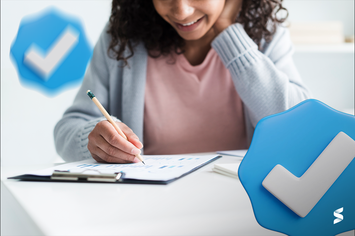 Pessoa sorrindo fazendo anotações em papel durante estudo para concurso público, com ícones de confirmação ao fundo