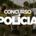 Dois policiais militares vistos por trás, com viatura ao fundo em uma rua.