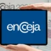 Imagem mostrando o logo do ENCCEJA 2025 em um tablet com fundo de documentos de inscrição