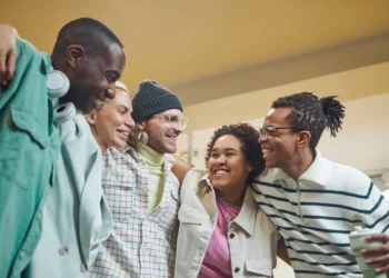 Grupo de amigos sorrindo e posando juntos em ambiente moderno, com roupas casuais e estilo descontraído.