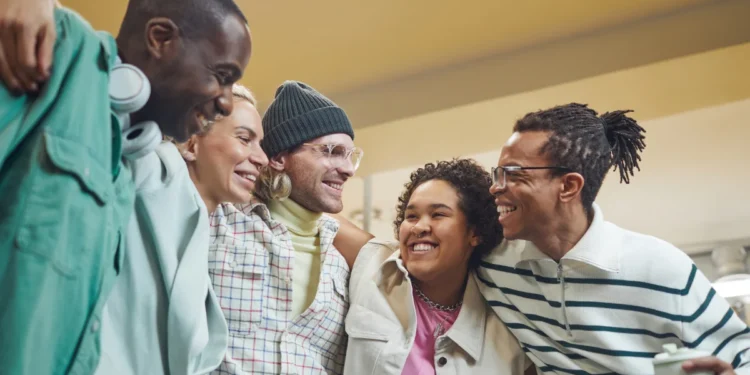 Grupo de amigos sorrindo e posando juntos em ambiente moderno, com roupas casuais e estilo descontraído.