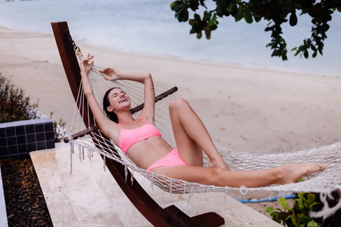 Mulher sorridente descansando em rede na praia, aproveitando as férias