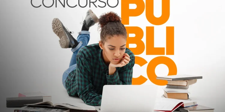 Jovem estudando para concurso público com laptop e livros ao redor.