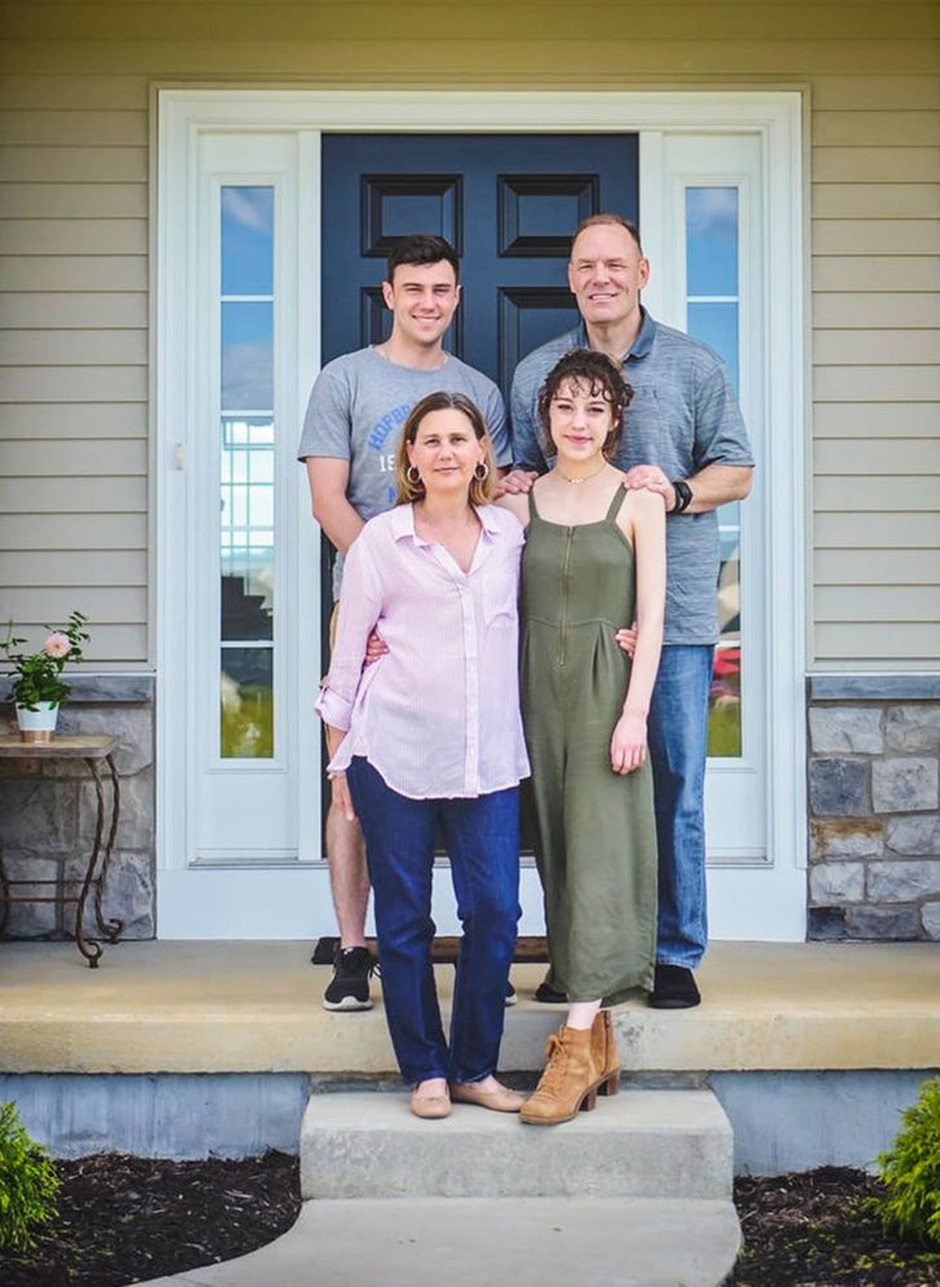 Desafio visual com uma família sorridente em frente à porta da casa, com dois adultos e dois jovens reunidos na entrada.