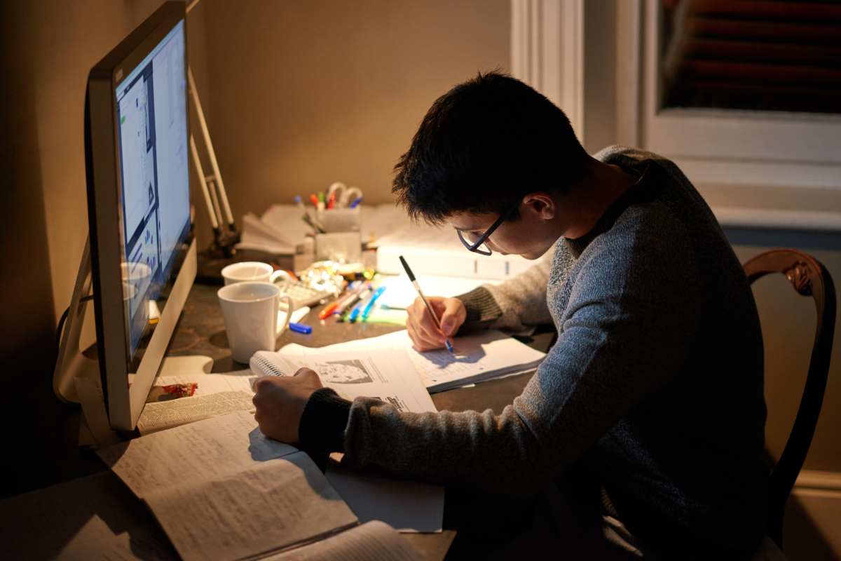 Estudante concentrado estudando à noite, com livros e canetas ao redor.