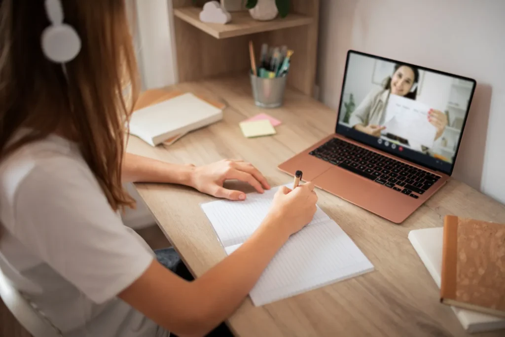  Aula online com estudante escrevendo em caderno durante explicação por vídeo chamada
